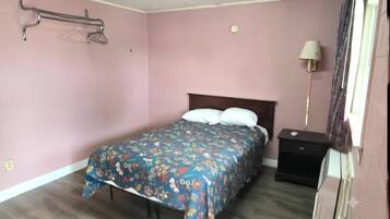 Un dormitorio con una cama, una mesita de noche, una lámpara y un estante en la pared.