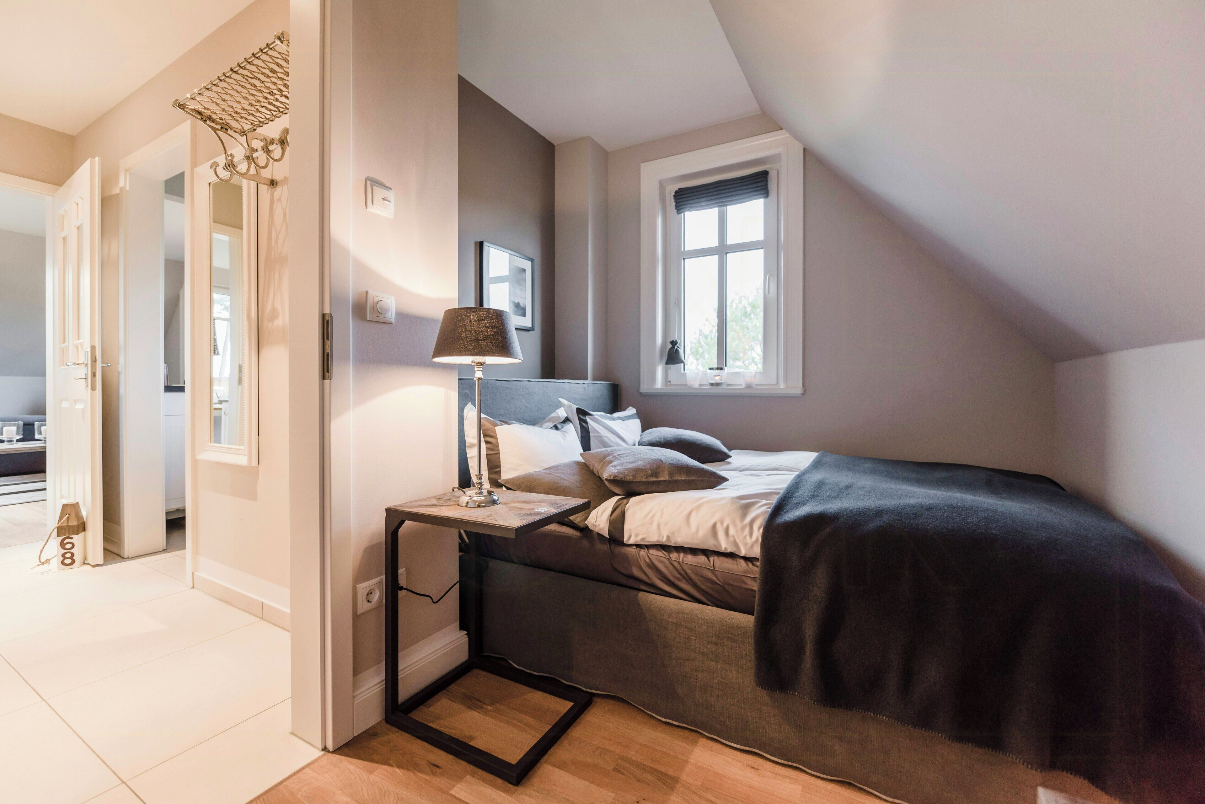 A bedroom with a bed, bedside table, lamp, window, and a door leading to another room.