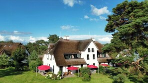 A large white building with a thatched roof, surrounded by greenery and red umbrellas. - Luxury apartment with water view in Loddin (Kamphof)