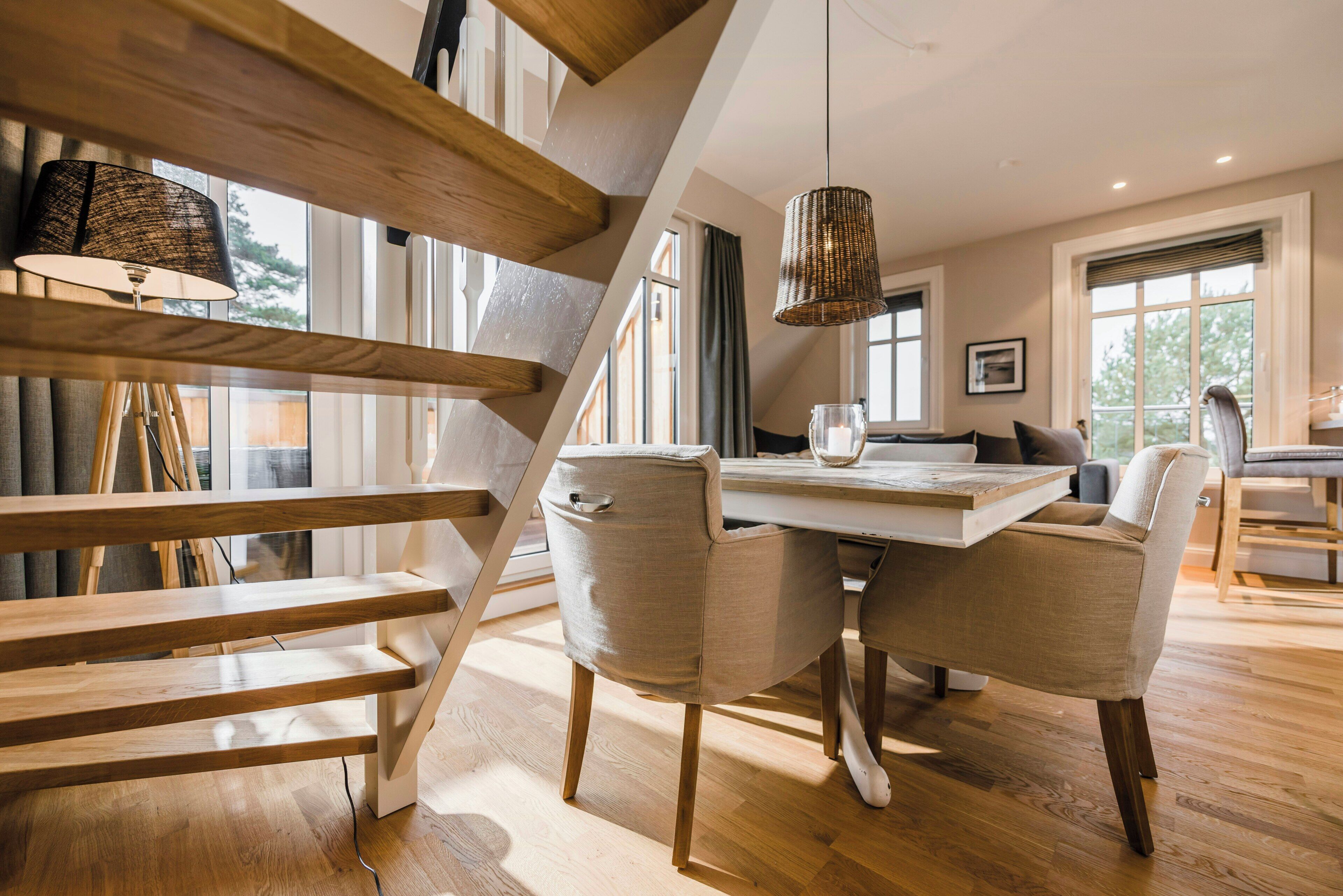 Een modern interieur met een houten trap, een eethoek met een tafel en stoelen, en grote ramen.