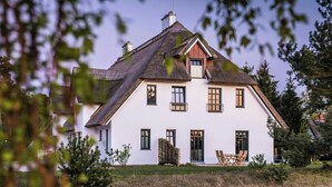 Una casa bianca con un tetto ripido, diverse finestre e un portico con sedie.