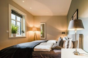Un dormitorio con cama, lámparas de noche, una ventana con persianas y un espejo.