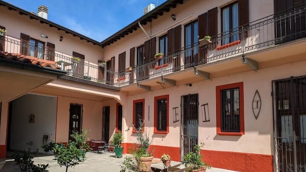 A two-story building with balconies, red-framed windows, and a courtyard with potted plants.