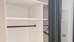 A white closet with shelves and a rod, a door with a handle, and a curtain.