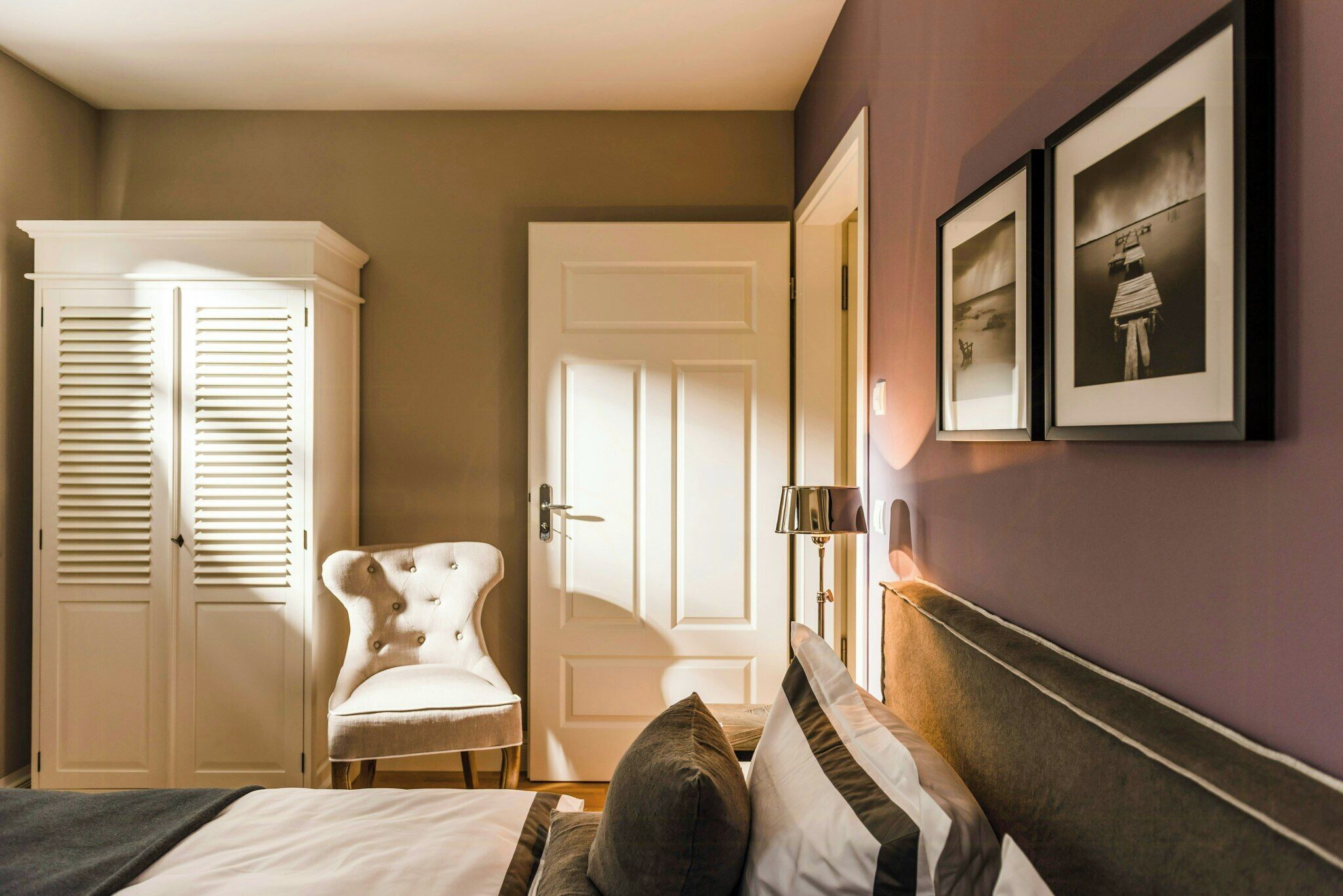 Een slaapkamer met een bed, een stoel, een kledingkast en twee foto's in lijsten aan de muur.