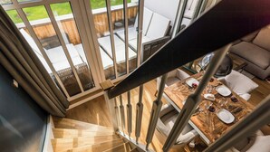 Ein modernes Interieur mit einer Holztreppe, einem Essbereich mit weißen Möbeln und Blick auf eine Terrasses.