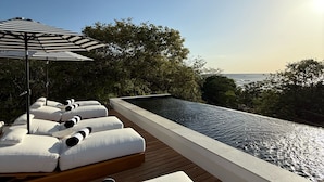 A rooftop infinity pool with white lounge chairs and a striped umbrella. - NOAM by the sea Ocean View Suite #4 Adults Only (Tamarindo)