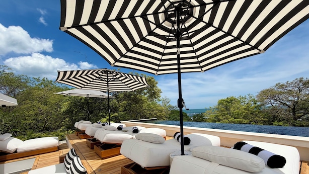 A deck with white lounge chairs and striped umbrellas, overlooking a body of water. - NOAM by the sea Ocean View Suite #4 Adults Only (Tamarindo)