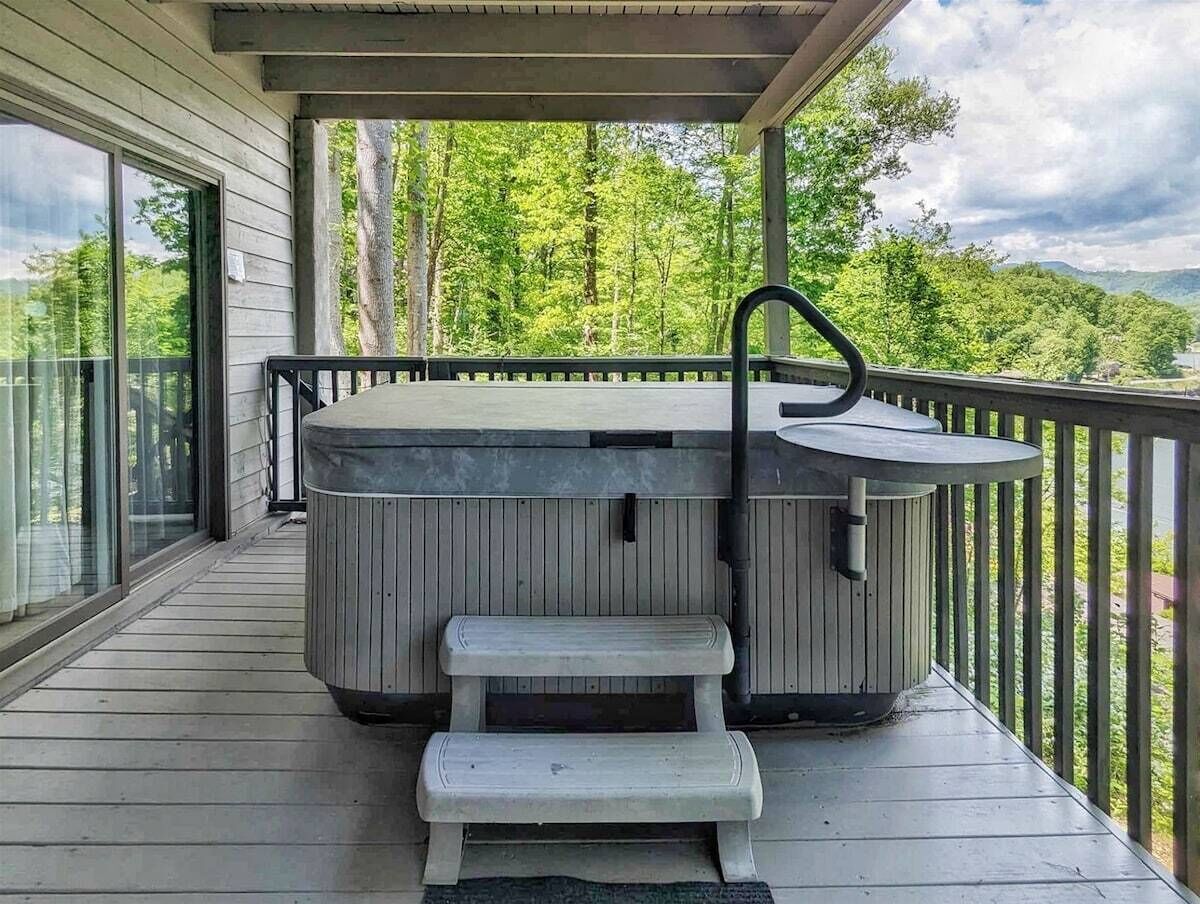 Ein Whirlpool auf einer Holzterrasse mit Blick auf Bäume und Hügel.
