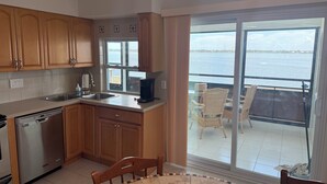 A kitchen with wooden cabinets, a dishwasher, a coffee maker, and a view of the sea through large sliding doors. - Waterfront Lemon Bay Condo 2 Bed & Full Kitchen -Private Beach Access Boat dock (Englewood)