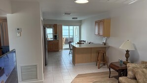 A modern kitchen with wooden cabinets, a central island, and a dining area with a sofa and a lamp. - Waterfront Lemon Bay Condo 2 Bed & Full Kitchen -Private Beach Access Boat dock (Englewood)