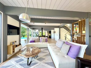 Un salon moderne avec un canapé blanc, une table basse en verre et un escalier menant à une mezzanine.
