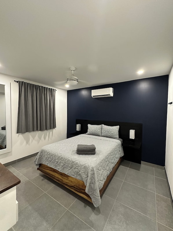A modern bedroom with a bed, bedside tables, a ceiling fan, and an air conditioning unit.