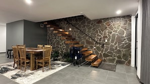 Un espace repas avec un mur en pierre, un escalier en bois et une table entourée de chaises.