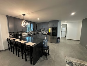 A modern kitchen with grey cabinets, a central island with bar stools, a stainless steel refrigerator, and a water dispenser.
