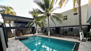 Une piscine extérieure moderne, dotée d’un revêtement de sol en pierre, entourée de palmiers et agrémentée d’un espace salon abrité.