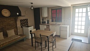 A compact kitchen with a dining area, a clock, a microwave, and a refrigerator.