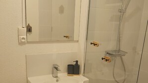 A bathroom with a toilet, sink, mirror, and glass-enclosed shower.