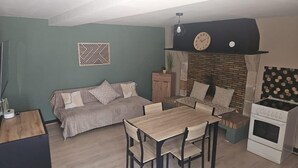 A cozy living room with a sofa, a dining table, chairs, a fireplace, and a kitchen area with an oven.
