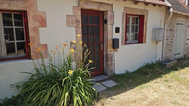 A house with a red door, a window with a red frame, and a small garden with yellow flowers.