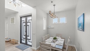 A dining area with a table set for four, a hanging light fixture, and a view of the outside through a door. - Siesta Swim House (Sarasota)
