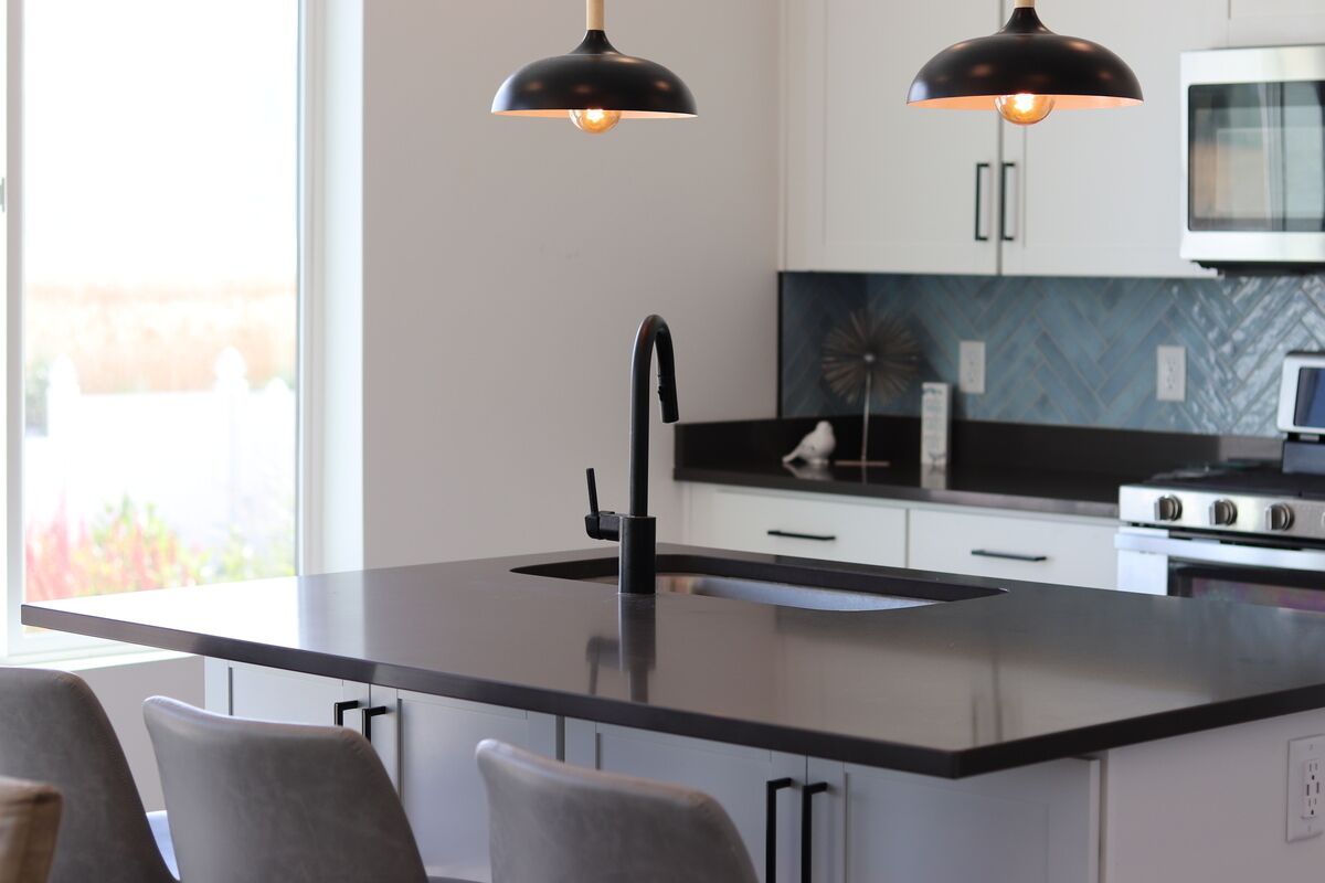 Een moderne keuken met een centraal eiland, zwarte hanglampen en uitzicht op de omgeving.