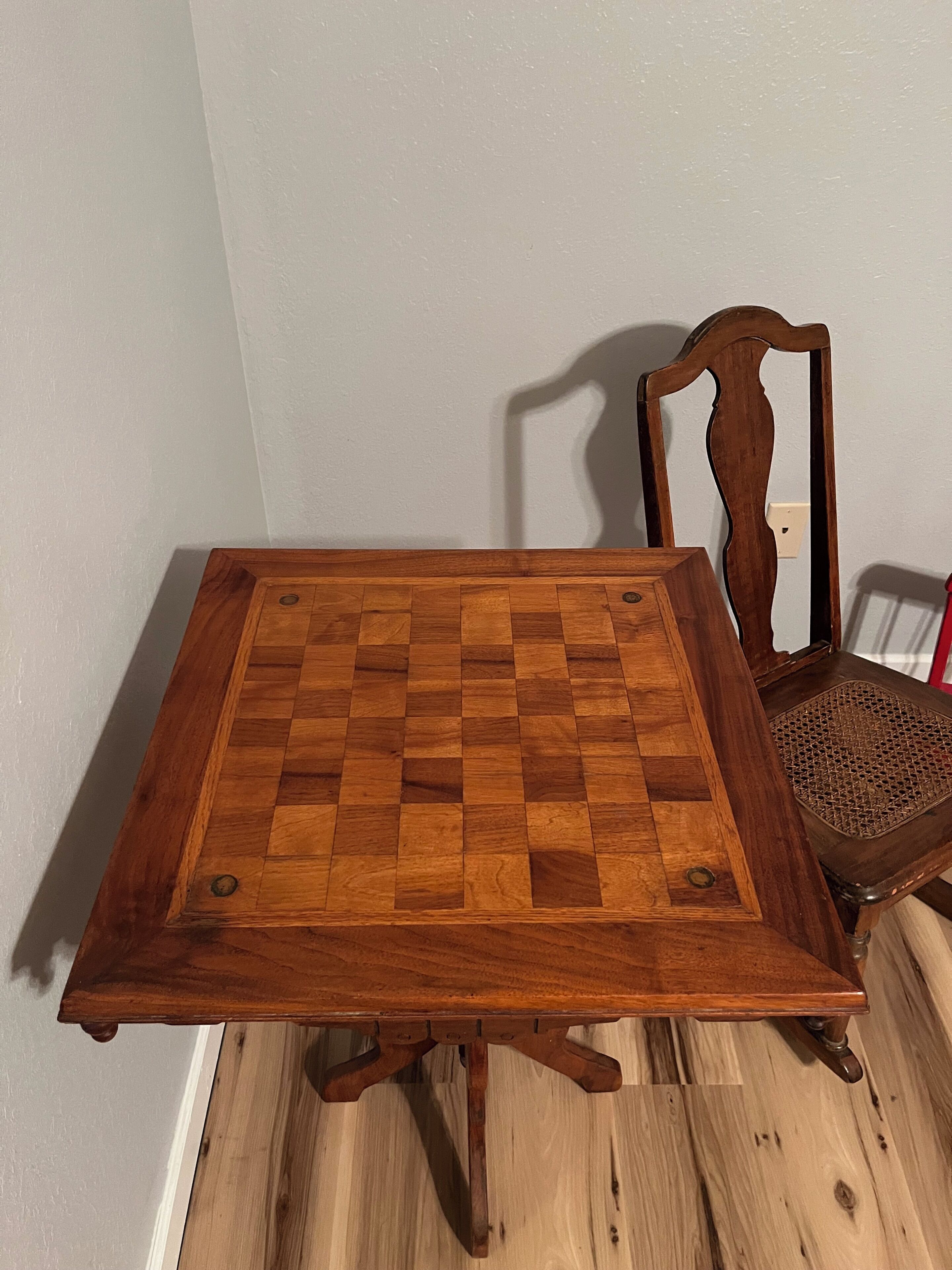 Una mesa de madera con superficie a cuadros, una silla con asiento tejido y una pared lisa de fondo.