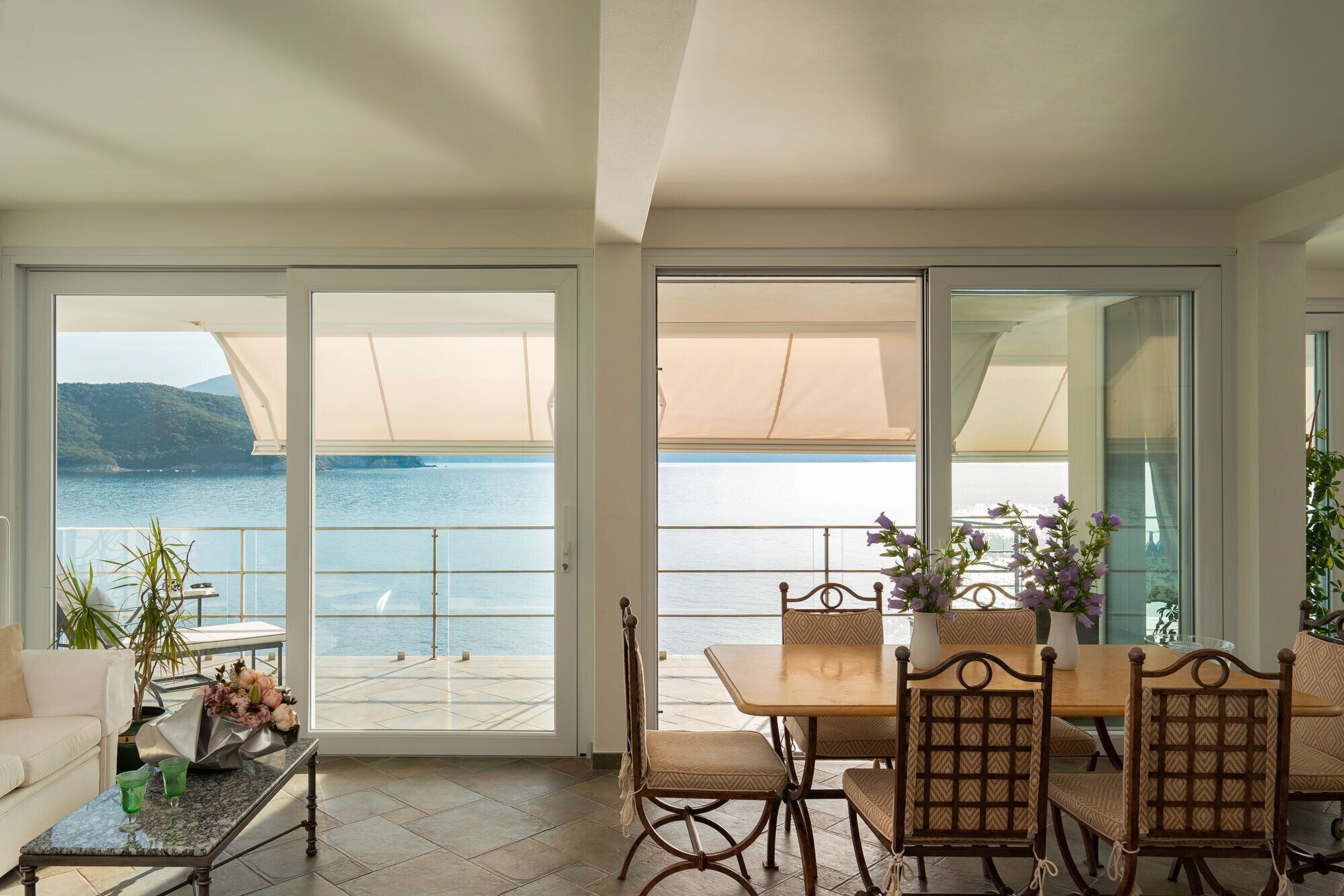 A balcony with a table and chairs, a sofa, and a view of the sea.