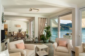 A spacious living area with a balcony overlooking a body of water, a dining area, and a television. - Villa Il Faro 10, Emma Villas (Scaglieri)