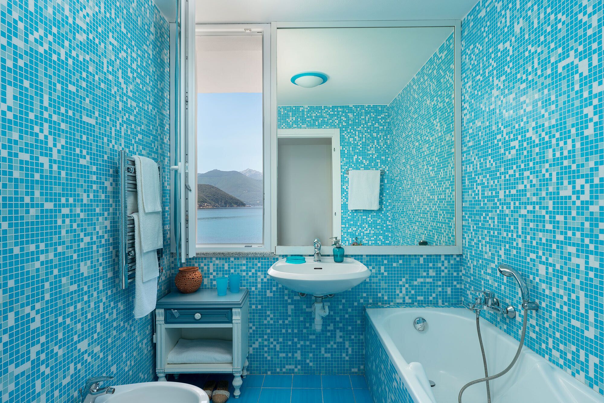 A bathroom with a view of the sea, a sink, a bathtub, and a mirror.