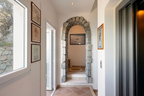 A hallway with stone archway, framed artwork, and a door with a metal handle. - Villa Il Faro 10, Emma Villas (Scaglieri)