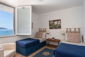 Ein Hotelzimmer mit zwei Betten, einem Schlafsofa, einem kleinen Tisch, einem Gemälde und Meerblick.