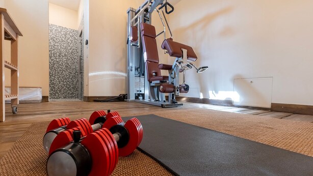 Une salle de sport équipée de matériel d’exercice, d’un tapis et d’un mur orné d’un motif décoratif.