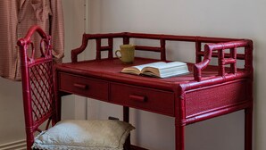 Un bureau en osier rouge sur lequel se trouvent un livre et une tasse, une chaise et un coussin posé sur le sol.