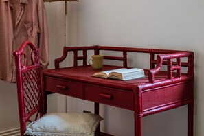 Ein roter Korbtisch mit einem Buch und einer Tasse darauf, ein Stuhl und ein Kissen auf dem Boden.
