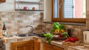 Une cuisine avec un mur recouvert de briques, des armoires en bois, un évier en acier inoxydable et une fenêtre avec des stores.
