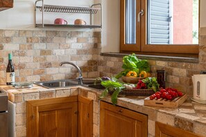 Eine Küche mit Ziegelrückwand, Holzausbau und einem Edelstahlspülbecken, sowie einem Fenster mit Jalousien.
