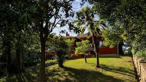 Un bâtiment rouge doté d’un balcon, entouré d’arbres et d’herbe.