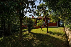 Ein rotes Gebäude mit Balkon, umgeben von Bäumen und Gras.