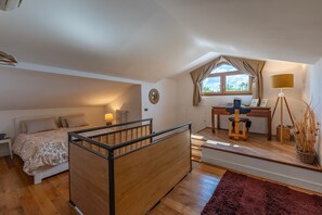 Ein Schlafzimmer mit einem Bett, einem Schreibtisch, einem Sessel, einer Lampe und einem Fenster.