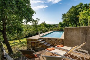 A swimming pool with stone steps, surrounded by trees and equipped with lounge chairs.