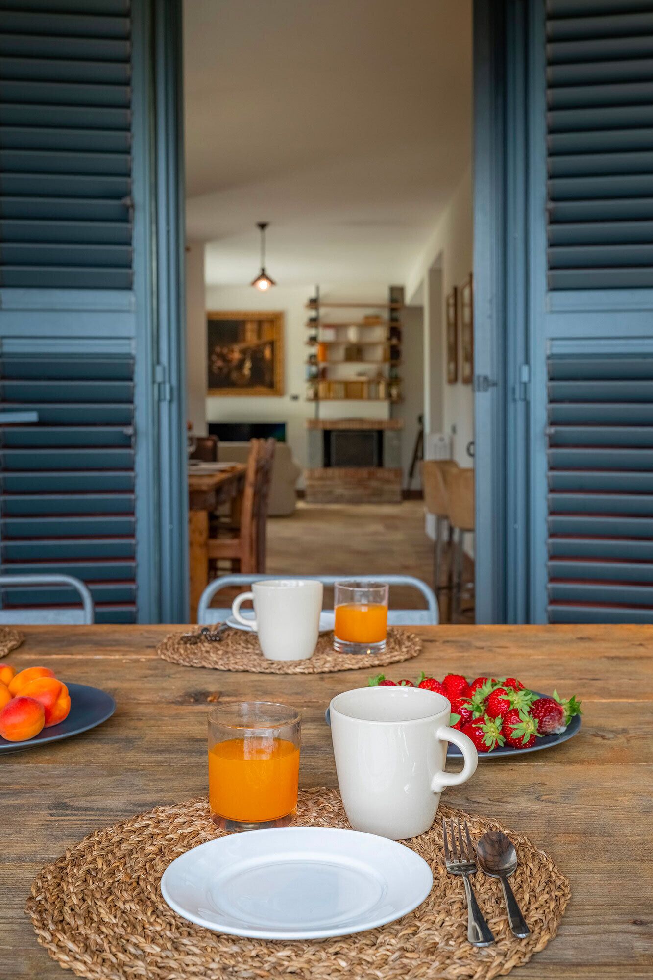 A breakfast table with a plate of strawberries, a glass of orange juice, and a white mug.