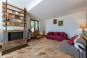 Un salon avec une cheminée, un canapé rouge, une bibliothèque et une fenêtre.
