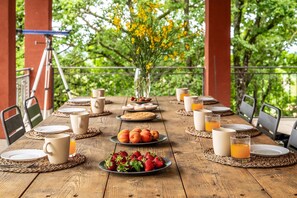 Ein Holztisch, gedeckt für ein Frühstück, mit Tellern, Tassen und einer Blumenvase.