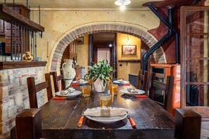 A dining area with a wooden table, chairs, a vase with plants, and a brick archway.