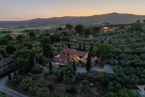 A villa with a swimming pool, surrounded by olive trees and hills.