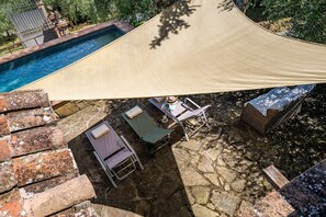 A poolside area with a canopy, lounge chairs, and a small table with a hat and book.