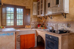 A rustic kitchen with a stone backsplash, wooden cabinets, a window with a view, and a built-in oven. - Colle Calzolaro 8, Emma Villas (Tavernelle)