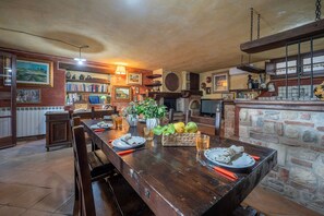 A rustic dining area with a wooden table, chairs, a vase with green plants, and a stone wall. - Colle Calzolaro 8, Emma Villas (Tavernelle)