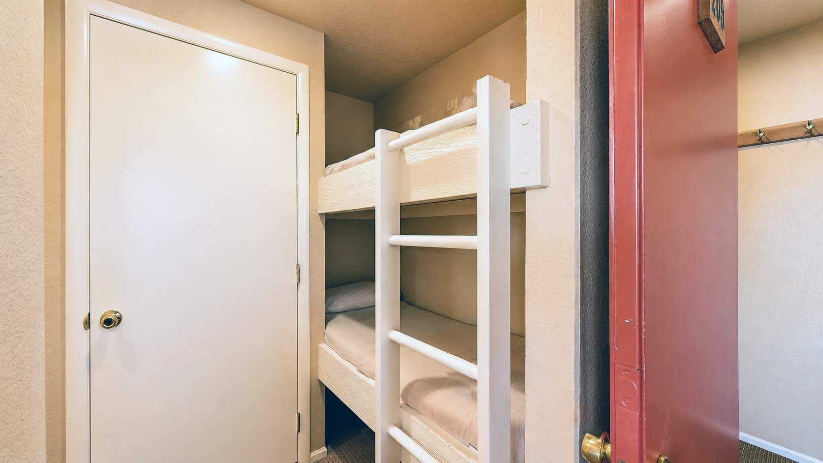 A room with a bunk bed, a door, and a red wall.